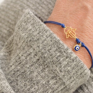 May include: A blue string bracelet with a gold hamsa hand charm and a blue evil eye charm.