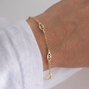 May include: A gold chain bracelet with a delicate design featuring multiple evil eye charms. The bracelet is shown on a person's wrist.