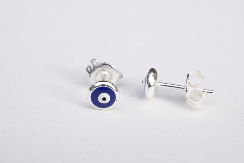 May include: A pair of silver earrings with a blue evil eye design. The earrings are small and delicate, and they would make a great gift for someone special.