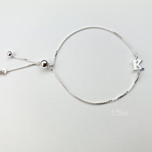 May include: A silver adjustable bracelet with a small silver charm in the shape of the letter K.