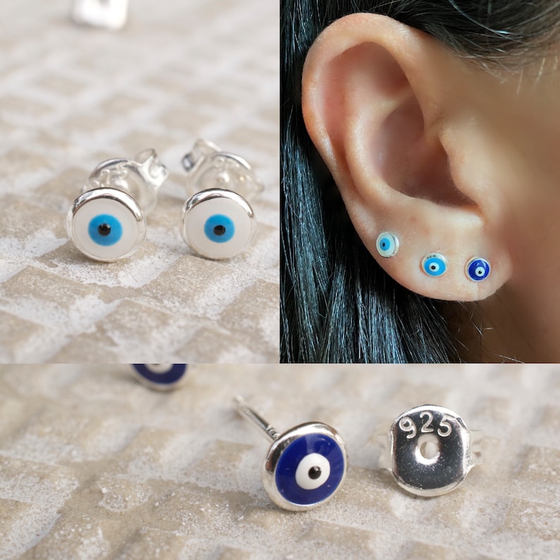 May include: A pair of sterling silver earrings with a blue evil eye design. The earrings are shown on a white background and on a model's ear. The earrings are also shown with a 925 stamp on the back.