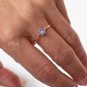 Peut inclure: Une bague en or avec un charme &oelig;il turc bleu et blanc. La bague est port&eacute;e sur un doigt.