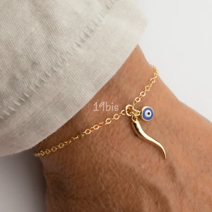 May include: Gold chain bracelet with a blue evil eye charm and a gold horn charm.