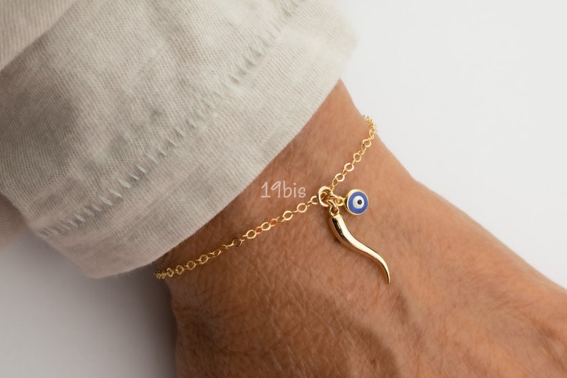 May include: Gold chain bracelet with a blue evil eye charm and a gold horn charm.