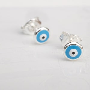May include: A pair of silver earrings with blue evil eye charms. The earrings are small and delicate, and the evil eye charms are a popular symbol of protection.