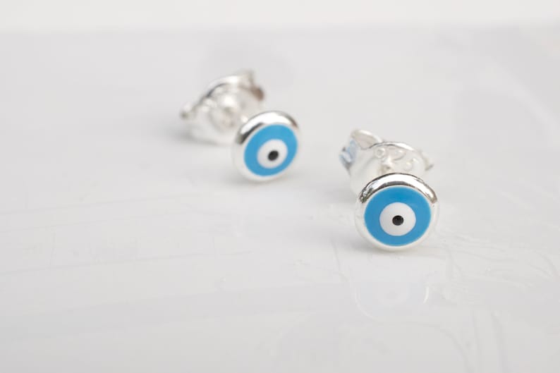 May include: A pair of silver earrings with blue evil eye charms. The earrings are small and delicate, and the evil eye charms are a popular symbol of protection.