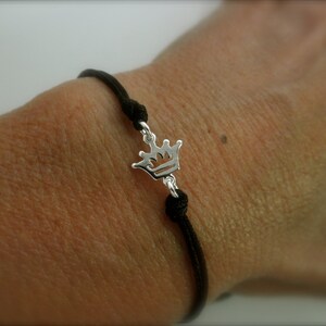 May include: A black string bracelet with a silver crown charm.