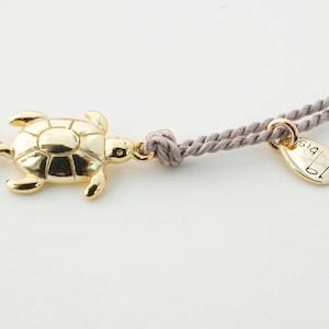 May include: A gold turtle charm on a gray cord bracelet with a gold tag that says "DIS".