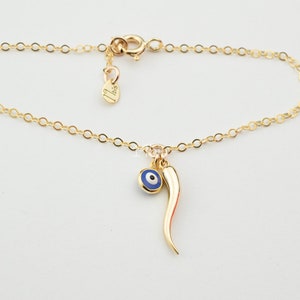 May include: Gold chain bracelet with a blue evil eye charm and a red chili pepper charm.