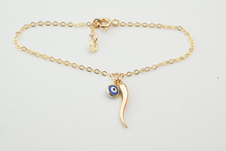 May include: Gold chain bracelet with a blue evil eye charm and a red chili pepper charm.