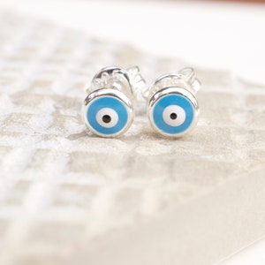 May include: A pair of silver earrings with blue evil eye charms. The earrings are small and delicate, and the evil eye charms are a popular symbol of protection.