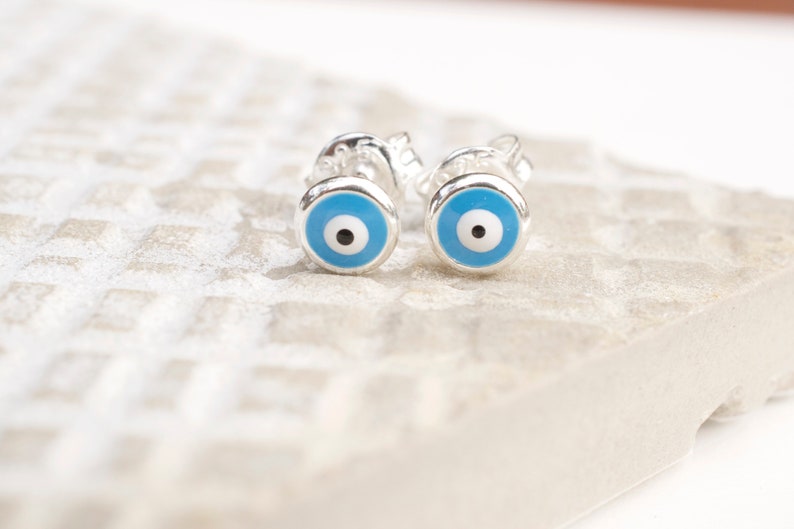May include: A pair of silver earrings with blue evil eye charms. The earrings are small and delicate, and the evil eye charms are a popular symbol of protection.