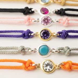 May include: A set of six colorful bracelets with different colored gemstones. Each bracelet is made of two strands of cord and features a small, round gemstone charm.