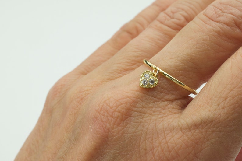 May include: A gold ring with a dangling heart charm. The heart is set with small clear stones.