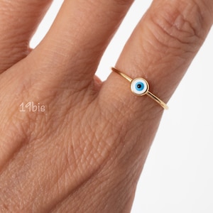 Peut inclure: Une bague en or avec un charme &oelig;il turc bleu et blanc. La bague est port&eacute;e &agrave; un doigt.