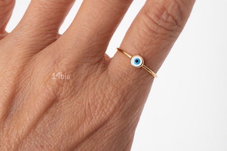 Peut inclure: Une bague en or avec un charme &oelig;il turc bleu et blanc. La bague est port&eacute;e &agrave; un doigt.