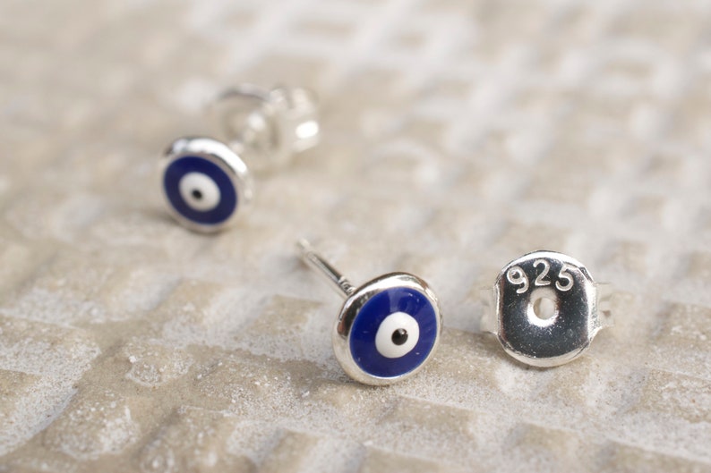 May include: A pair of sterling silver earrings with blue evil eye charms. The earrings are marked with "925" on the back.