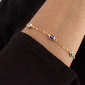 May include: A gold chain bracelet with four blue and white evil eye charms. The bracelet is on a person's wrist.