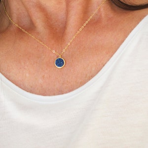 May include: A gold chain necklace with a small, round pendant. The pendant is blue and has a sparkly, textured surface.