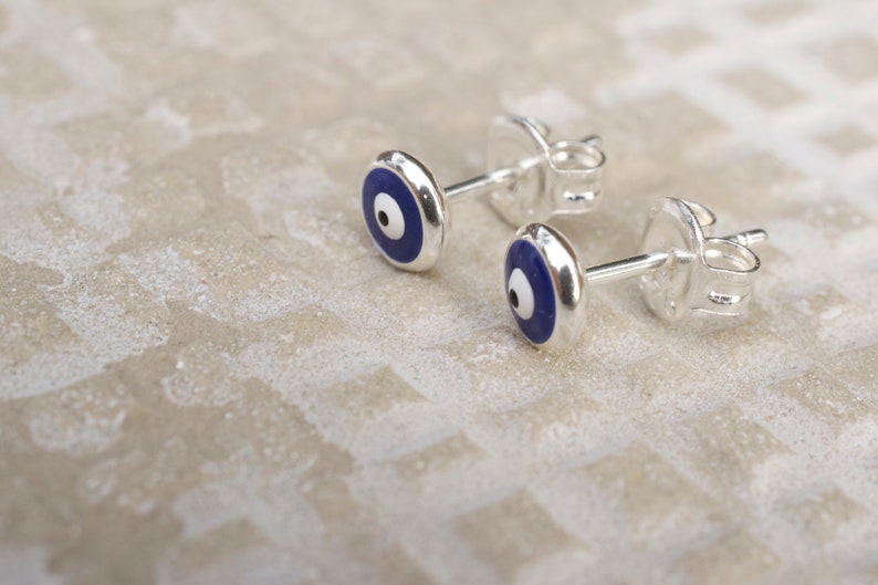 May include: A pair of silver earrings with blue and white evil eye charms. The earrings are a popular symbol of protection and good luck.