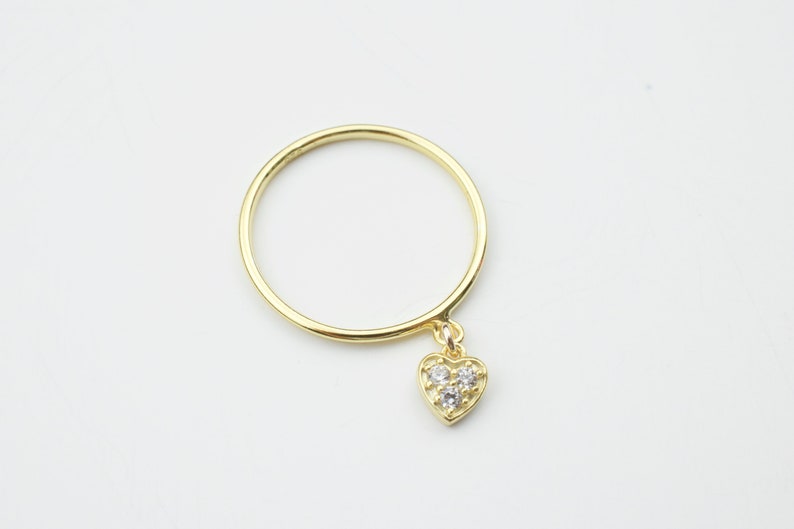 May include: A gold ring with a small, dangling heart charm. The heart charm has three small, clear stones.