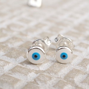 May include: A pair of silver earrings with blue and black evil eye charms.