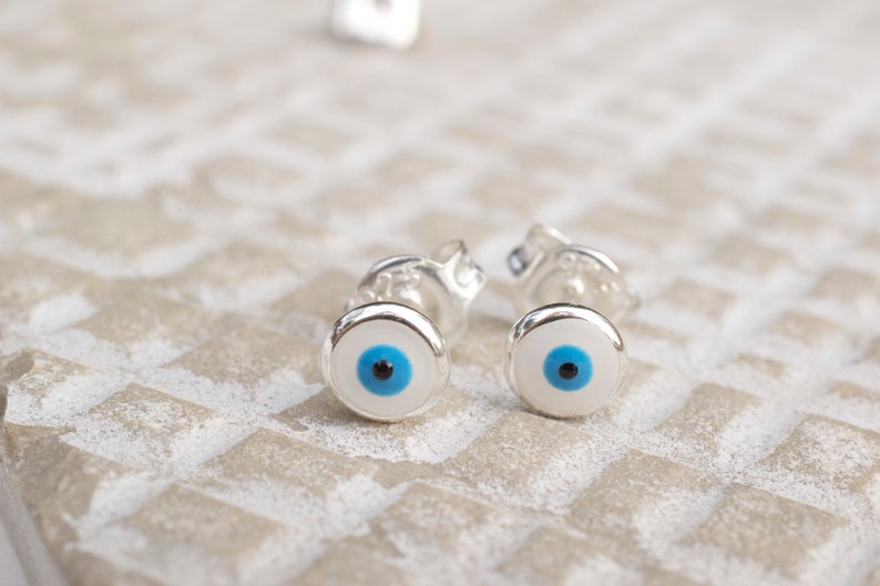 May include: A pair of silver earrings with blue and black evil eye charms.