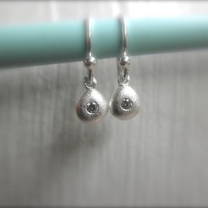 May include: A pair of silver earrings with a small diamond in the center of each earring.