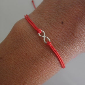 May include: Red string bracelet with a silver infinity symbol charm.