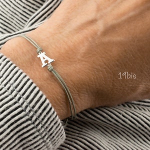 May include: A gray cord bracelet with a silver charm in the shape of the letter A.