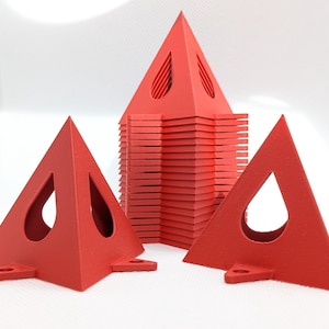 May include: A collection of bright red, triangular objects with a geometric design. Each piece has a cutout shape and small feet. The objects are stacked and arranged on a white background, showcasing their vibrant color and unique form.