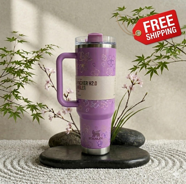 May include: A lavender Stanley Quencher H2.0 Flowstate tumbler with a handle, decorated with a floral pattern. The tumbler has a clear lid and a silver base. The text "Quencher H2.0 Tumbler" is visible on the side.