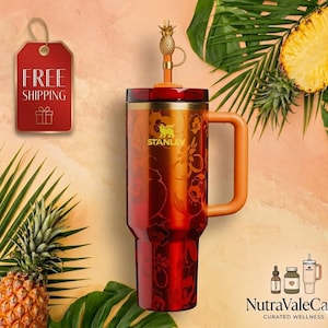 Pode incluir: Um copo Stanley vermelho e laranja com uma al&ccedil;a e uma tampa de canudo em forma de abacaxi. O copo tem um design floral e o logotipo da Stanley. Uma etiqueta vermelha com "FRETE GR&Aacute;TIS" &eacute; vis&iacute;vel.