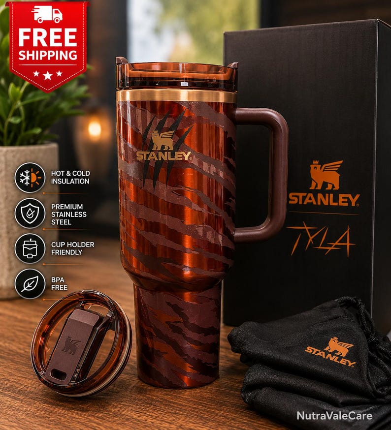 May include: A brown and copper-toned Stanley tumbler featuring a tiger-stripe pattern and claw mark graphics. The insulated cup includes a matching lid, a sturdy side handle, and is presented alongside a black branded box and a small black pouch.