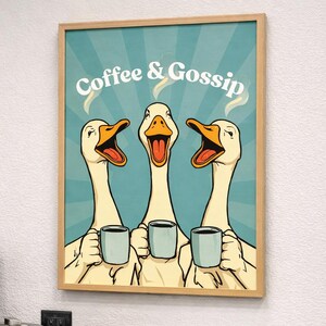 Könnte beinhalten: Ein gerahmter Druck mit drei Cartoon-Gänsen, die Kaffeetassen halten, mit dem Text "Coffee & Gossip". Die Gänse haben offene Schnäbel und Dampf steigt aus ihren Tassen auf. Der Druck wird über einer Kaffeemaschine und Zubehör angezeigt.