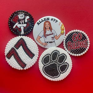 May include: Five circular pinback buttons. One features a bulldog mascot, one shows a softball player with the text ALLEN #77, one displays GO BULLDOGS, one has the number 77 in red crystals, and one features a black crystal paw print, all with pearl borders.