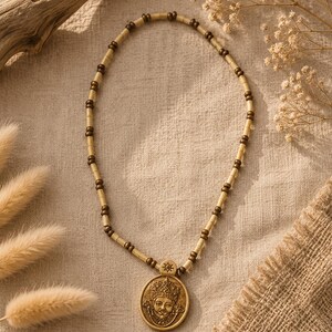 Peut inclure: Un collier de perles avec un pendentif circulaire. Le pendentif représente un visage détaillé avec une couronne. Le collier alterne des perles marron clair et foncé. Le fond est un tissu beige neutre.