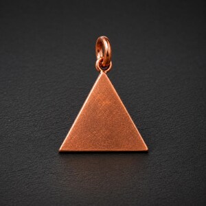 Può includere: Un ciondolo in metallo color rame a forma di triangolo equilatero. La superficie del triangolo presenta una finitura opaca leggermente testurizzata. Sulla punta superiore del triangolo è presente un piccolo anello di giunzione circolare.