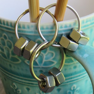 May include: A silver key chain with multiple rings and hexagonal nuts as charms. The keychain is hanging on the handle of a turquoise mug.