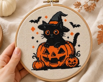May include: A circular wooden embroidery hoop containing a cross-stitch design on beige fabric. The design features a black cat wearing a witch hat, sitting inside a large orange jack-o'-lantern, flanked by two smaller pumpkins and bats.