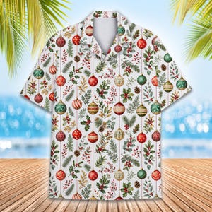 May include: A short-sleeve button-down shirt with a white background featuring a repeating pattern of colorful Christmas ornaments, green pine branches, holly leaves, red berries, and brown pinecones arranged in vertical lines across the fabric.