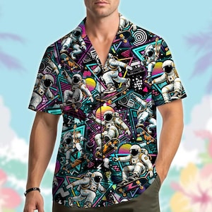 Puede incluir: Una camisa de manga corta con botones que presenta un patrón vibrante y repetitivo de astronautas en patineta sobre un fondo negro lleno de formas geométricas de neón, triángulos y patrones circulares en tonos rosa, azul y amarillo.