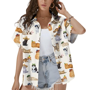 May include: A short-sleeved button-down shirt in an off-white color featuring an all-over print of various cats wearing different hats, including sombreros, berets, and beanies, along with some cats wearing fruit-themed headwear accessories.