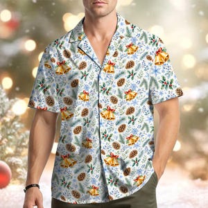 May include: A short-sleeved button-down shirt featuring a white background with a repeating holiday pattern of gold bells with red bows, brown pinecones, green pine needles, holly leaves with red berries, and light blue snowflakes.