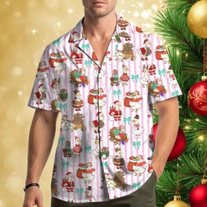 Puede incluir: Una camisa de manga corta con botones que presenta un patrón repetitivo de patos de dibujos animados vestidos con ropa navideña, incluyendo gorros de Papá Noel y bufandas, entre regalos y lazos azul turquesa sobre rayas verticales rosas.