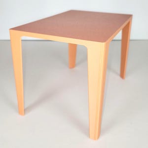 May include: A small, square table in a solid peach color. The table has a flat top and four straight legs. The table is approximately 24 inches tall, 18 inches wide, and 18 inches deep.