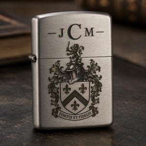 以下が含まれることがあります： 上部に「-JCM-」のイニシャルが刻まれた、つや消しシルバーのライター。イニシャルの下には、ライオン、ヘルメット、フルール・ド・リスが描かれた詳細な紋章があります。「FORTIS ET FIDELIS」の文字がデザインの下部にあります。