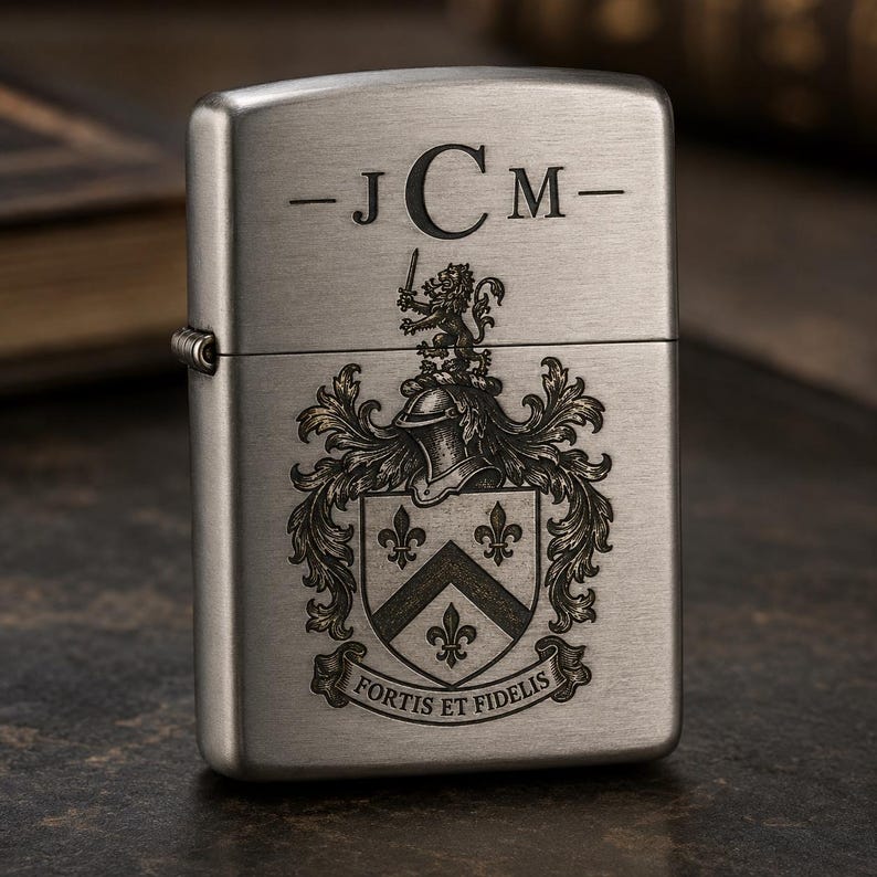 以下が含まれることがあります： 上部に「-JCM-」のイニシャルが刻まれた、つや消しシルバーのライター。イニシャルの下には、ライオン、ヘルメット、フルール・ド・リスが描かれた詳細な紋章があります。「FORTIS ET FIDELIS」の文字がデザインの下部にあります。