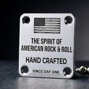 May include: A silver metal guitar neck plate with the American flag and the text "THE SPIRIT OF AMERICAN ROCK & ROLL HAND CRAFTED SINCE DAY ONE." Four screw holes are in each corner. Three screws are visible.