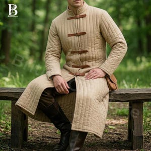 May include: A beige quilted coat with brown leather straps and a high collar. The long coat features vertical stitching and is fastened with three leather buckles. A small brown pouch hangs at the waist. The coat is knee-length.